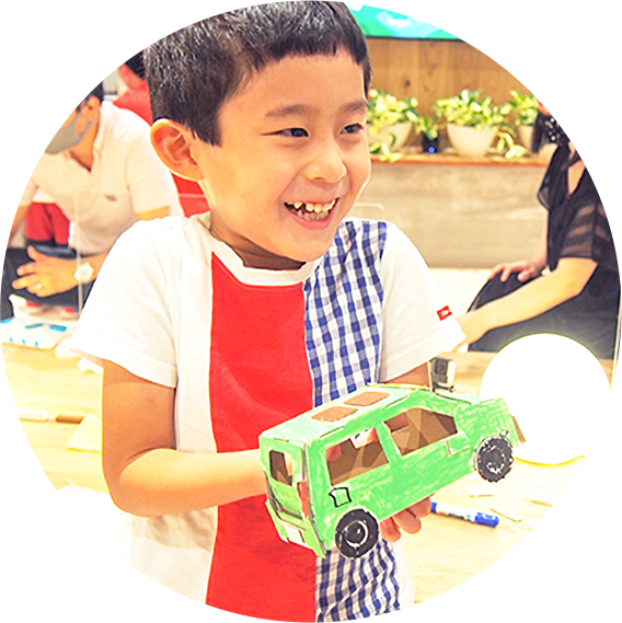男の子が笑顔でダンボールクラフトで作成したクルマを持つ様子