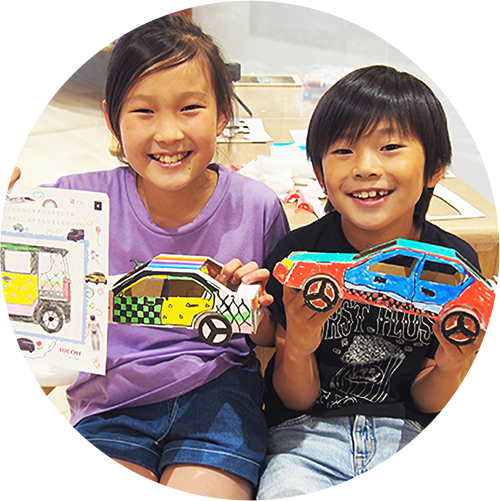 男の子と女の子がダンボールのクルマを笑顔で掲げる様子